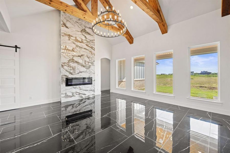 Unfurnished living room featuring a high ceiling, a chandelier, beamed ceiling, arched walkways, and a high end fireplace Unfurnished living room featuring a high ceiling, a chandelier, beamed ceiling, arched walkways, and a high end fireplace