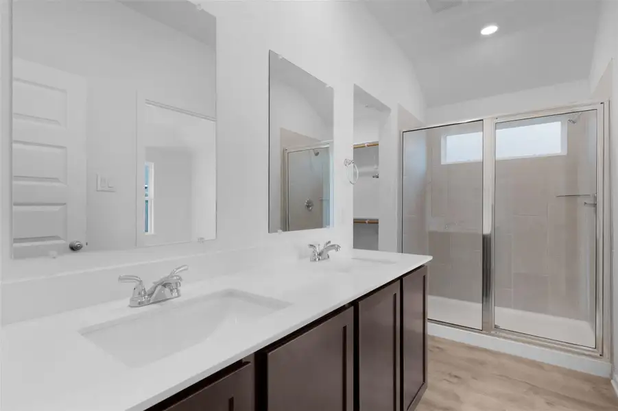Bathroom featuring double vanity, a shower stall, light wood finished floors, a spacious closet, and lofted ceiling