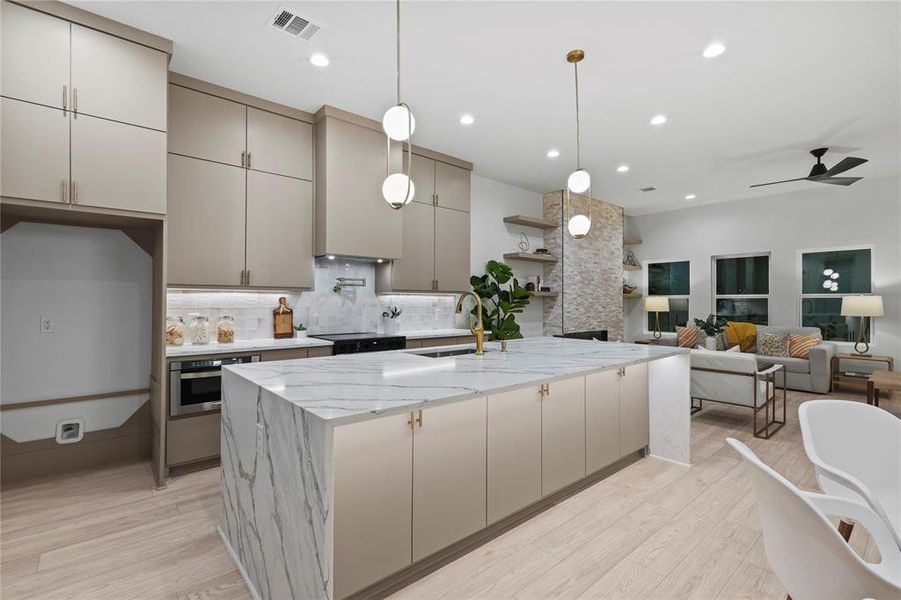 Kitchen featuring sink, tasteful backsplash, an island with sink, oven, and light hardwood / wood-style floors