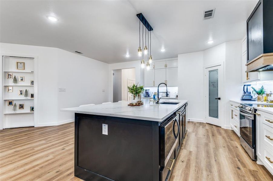 Kitchen with dark cabinetry, decorative light fixtures, white cabinetry, a center island with sink, and recessed lighting