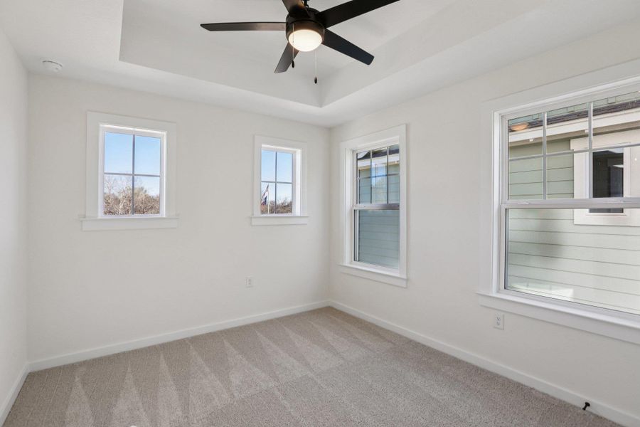 Empty room featuring light carpet, a tray ceiling, and a ceiling fan