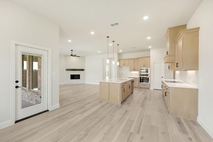 Open-concept kitchen and living area with light wood cabinets, center island, and fireplace visible in background