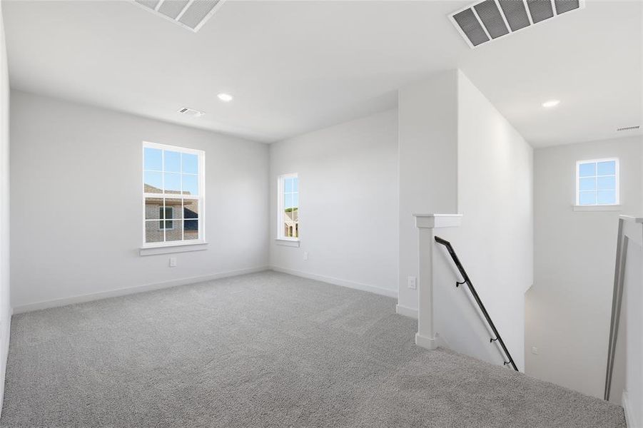 Carpeted loft area featuring two windows, recessed lighting, and a contemporary stair railing with black metal spindles and white newel posts