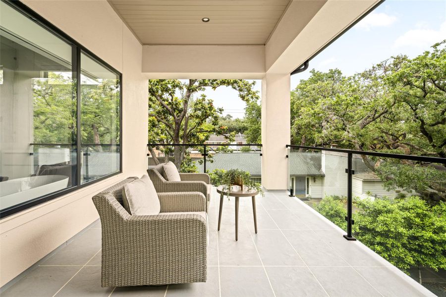Covered balcony off the primary suite with glass railing and treetop views.