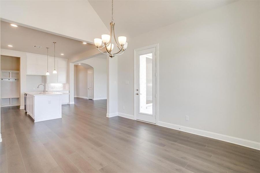 Unfurnished living room with sink, hardwood / wood-style flooring, lofted ceiling, and a notable chandelier