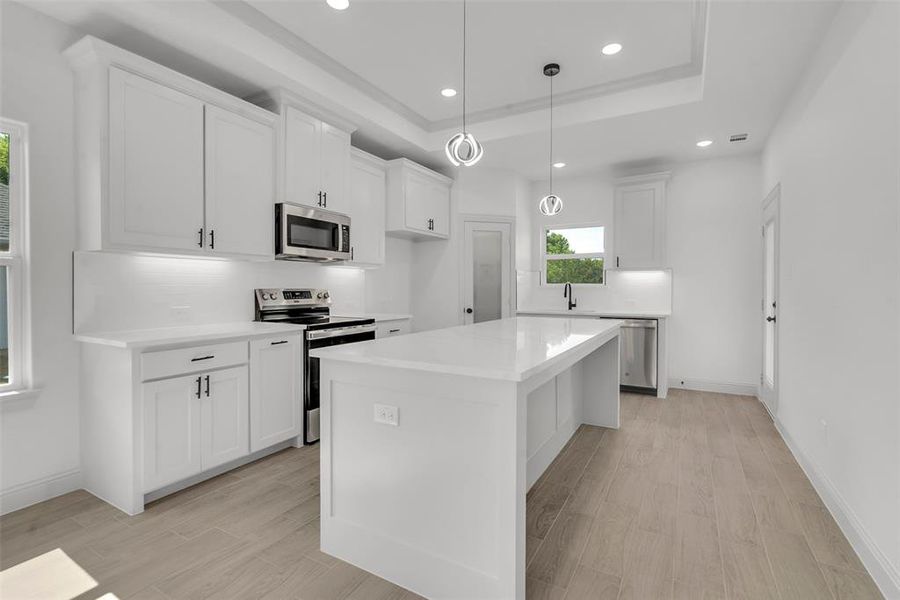 Kitchen featuring stainless steel appliances, recessed lighting, light countertops, light wood-type flooring, and white cabinets Kitchen featuring stainless steel appliances, recessed lighting, light countertops, light wood-type flooring, and white cabinets