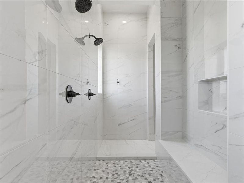 Walk-in shower with large-format white tile walls featuring subtle gray veining, dual showerheads in a matte black finish, and integrated wall niches