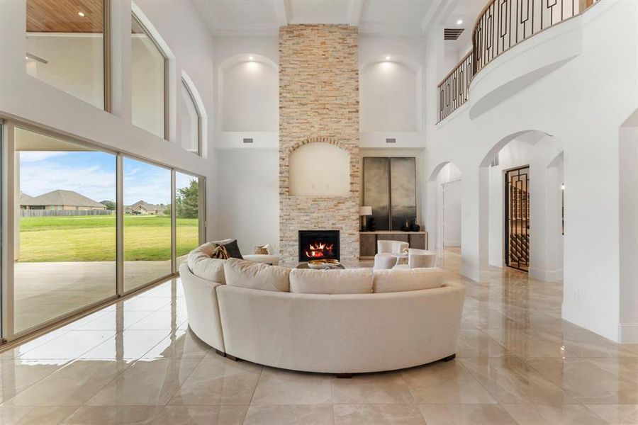 Another view to showcase the high coffered ceilings, stately stone fireplace, open staircase, and expansive floor-to-ceiling sliding windows that offer an abundance of natural light, picturesque view, and seamless indoor to outdoor entertaining.