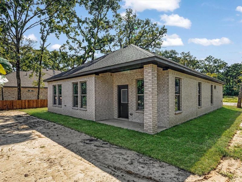 Rear view of property with brick siding, a patio area, and roof with shingles