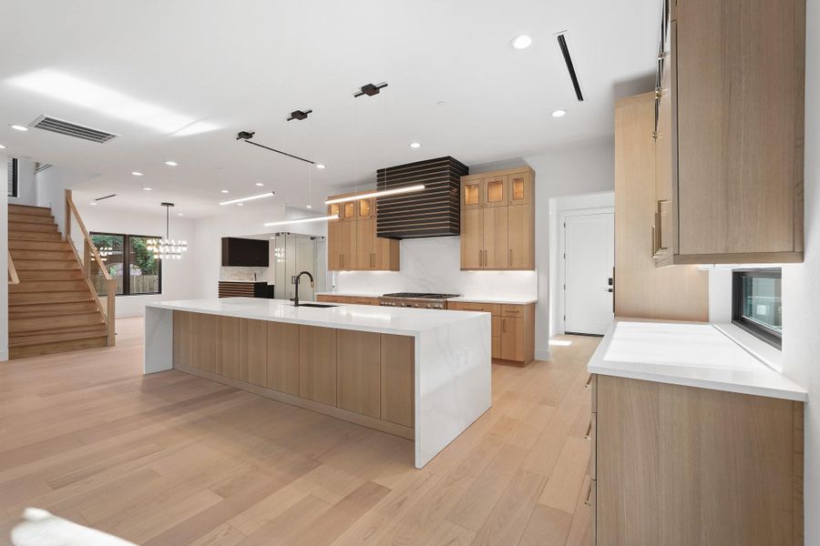 The clean and balanced design follows forward into the Kitchen accented with a layered look in the overhead vent cover and well-lit spaces. The far door to the right leads into the high ceiling garage.