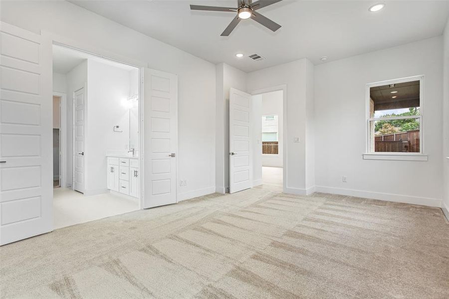 Unfurnished bedroom with ensuite bathroom, ceiling fan, and light colored carpet