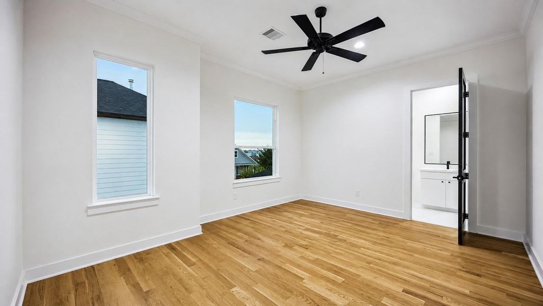 This bright bedroom offers a clean, modern retreat with warm wood flooring, crown molding, recessed lighting, and a bold black ceiling fan. Two windows bring in natural light and pleasant neighborhood views, while the adjoining bathroom adds privacy and convenience. The spacious layout allows flexibility for a complete bedroom suite, seating area, or workspace. This bright bedroom offers a clean, modern retreat with warm wood flooring, crown molding, recessed lighting, and a bold black ceiling fan. Two windows bring in natural light and pleasant neighborhood views, while the adjoining bathroom adds privacy and convenience. The spacious layout allows flexibility for a complete bedroom suite, seating area, or workspace.