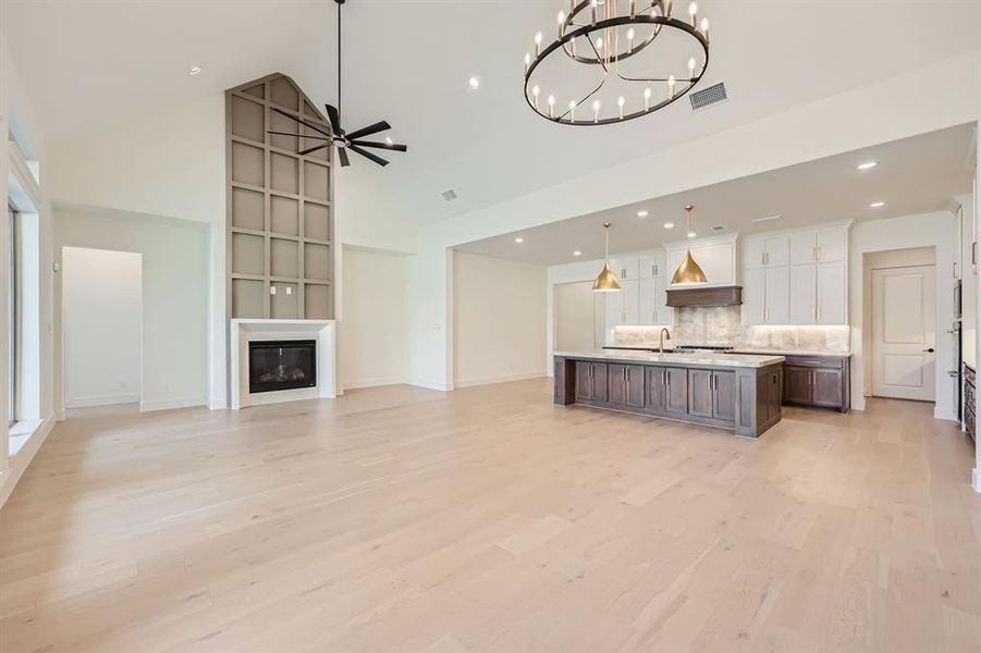 Kitchen featuring white cabinetry, pendant lighting, high vaulted ceiling, light hardwood / wood-style flooring, and a kitchen island with sink