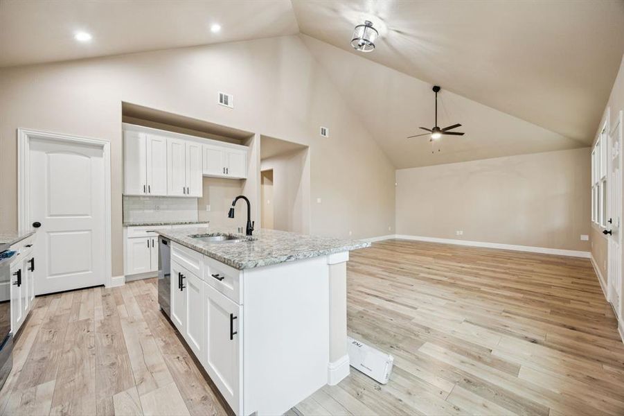 Kitchen featuring white cabinets, light stone countertops, tasteful backsplash, a center island with sink, and light wood finished floors Kitchen featuring white cabinets, light stone countertops, tasteful backsplash, a center island with sink, and light wood finished floors