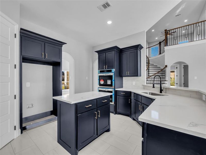 Kitchen with arched walkways, a kitchen island, double oven, light stone countertops, and tasteful backsplash Kitchen with arched walkways, a kitchen island, double oven, light stone countertops, and tasteful backsplash