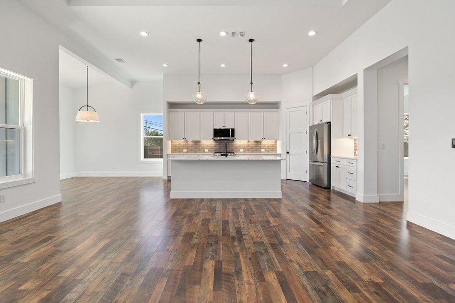 Kitchen with white cabinetry, hanging light fixtures, a kitchen island with sink, backsplash, and stainless steel appliances