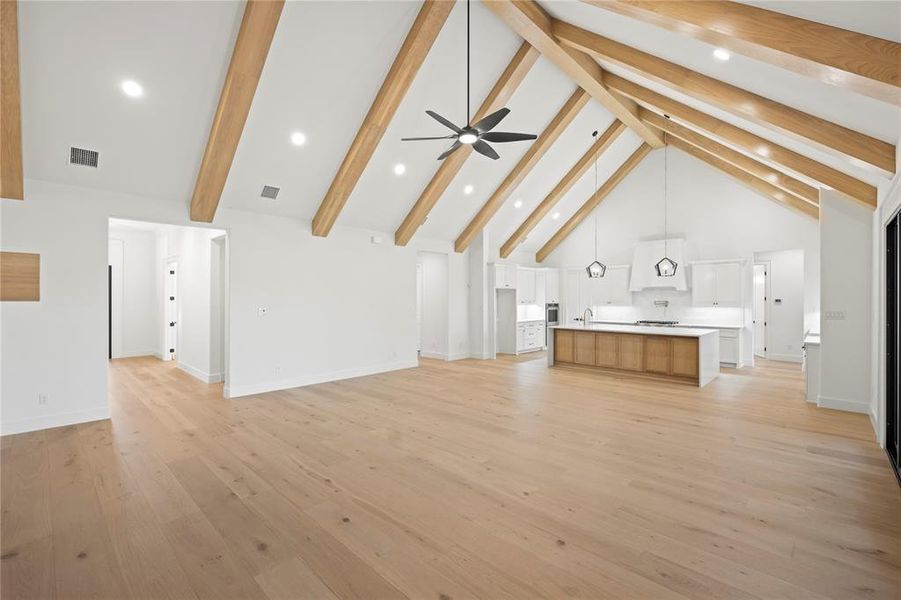 Expansive open-concept living space featuring a vaulted ceiling with exposed wood beams, recessed lighting, and a contemporary ceiling fan
