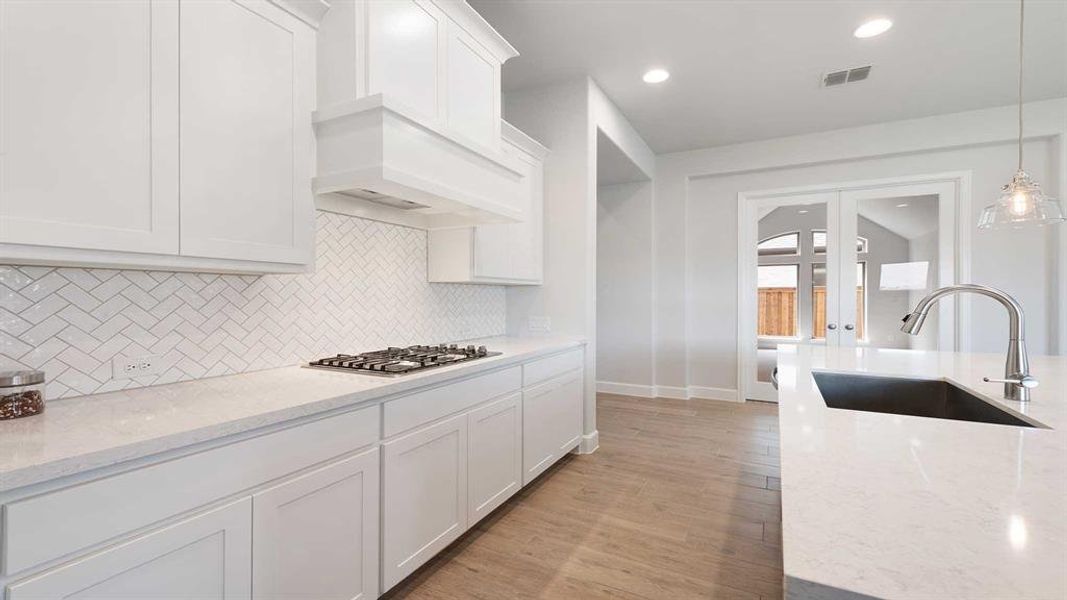 Kitchen featuring light wood-type flooring, stainless steel gas cooktop, sink, and light stone countertops