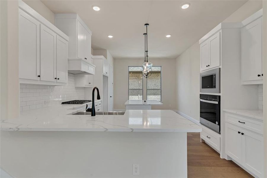 Kitchen with appliances with stainless steel finishes, light hardwood / wood-style flooring, backsplash, light stone countertops, and white cabinetry