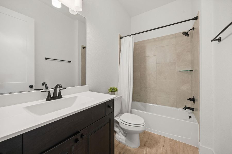 This bath includes a tiled tub surround, built-in glass shelf, and updated matte black fixtures.