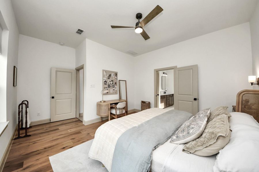 Primary bedroom with warm hardwood floors and modern ceiling fan.