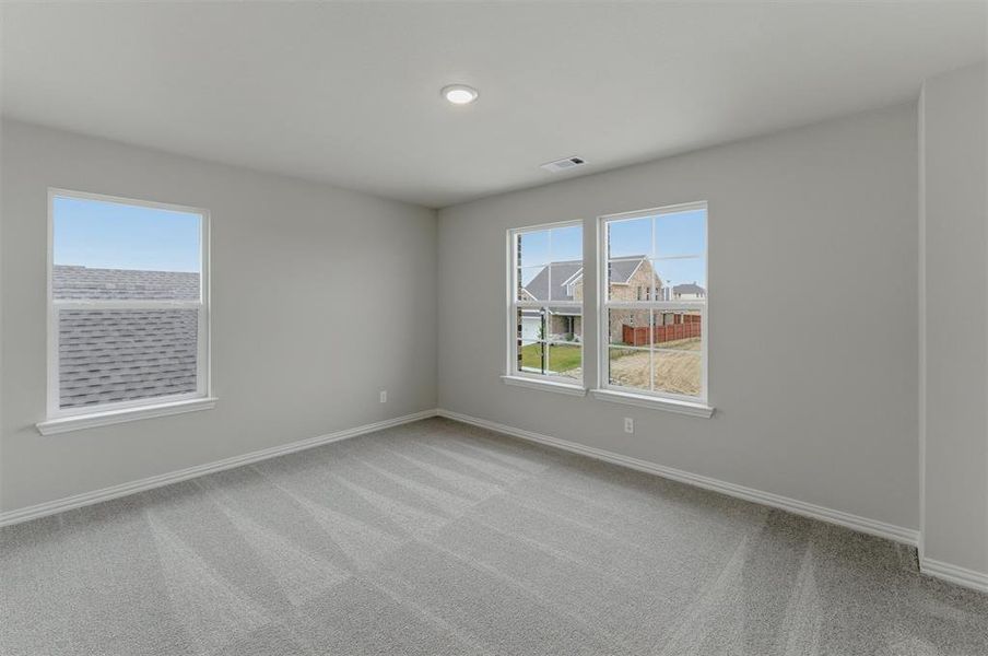 Spacious interior room featuring light gray carpeting, multiple windows with white trim, and recessed ceiling lighting