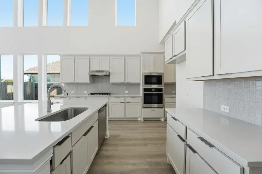 Kitchen featuring stainless steel appliances, light wood-style floors, backsplash, white cabinetry, and a towering ceiling