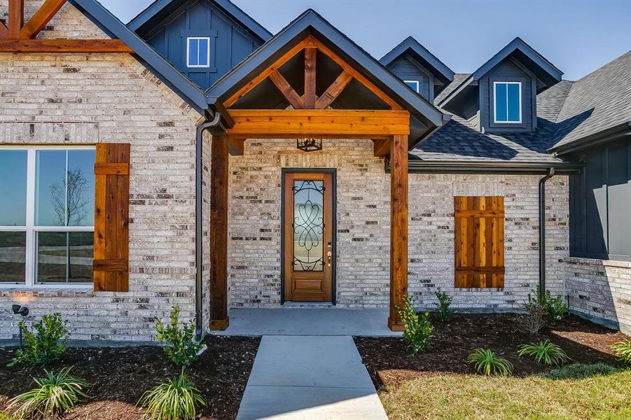View of exterior entry with board and batten siding, brick siding, covered porch, and roof with shingles View of exterior entry with board and batten siding, brick siding, covered porch, and roof with shingles