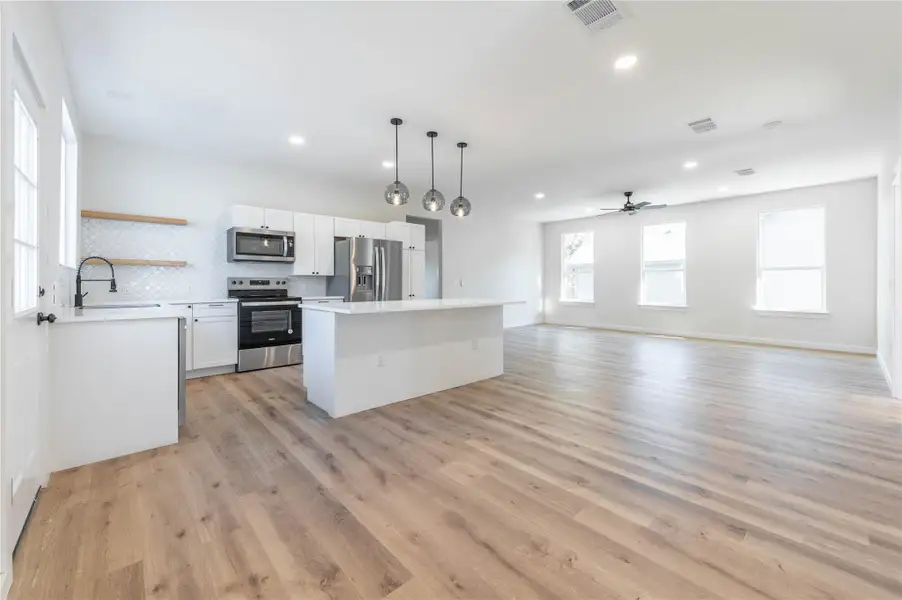 Kitchen featuring backsplash, stainless steel appliances, a kitchen island, light countertops, and open shelves