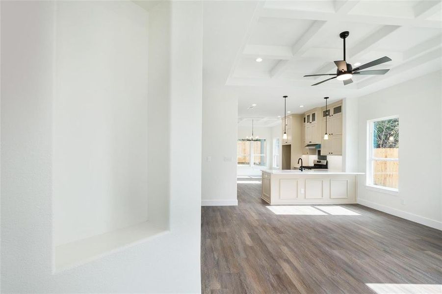 Unfurnished living room with coffered ceiling, dark wood finished floors, suspended lighting, and a ceiling fan