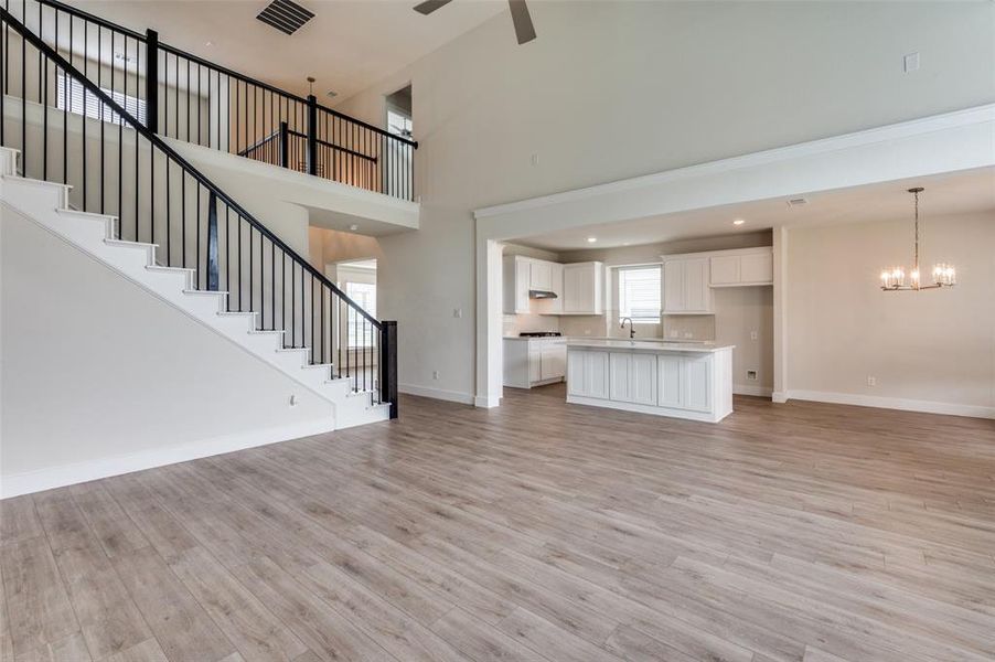 Unfurnished living room with a chandelier, a ceiling fan, baseboards, light wood finished floors, and stairway Unfurnished living room with a chandelier, a ceiling fan, baseboards, light wood finished floors, and stairway