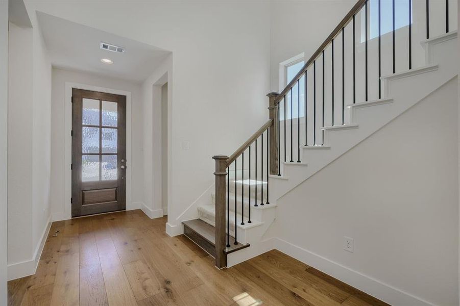Entryway with wood-finish flooring, a dark wood-paneled front door with textured glass, and a staircase featuring wood newel posts, iron balusters, and carpeted treads