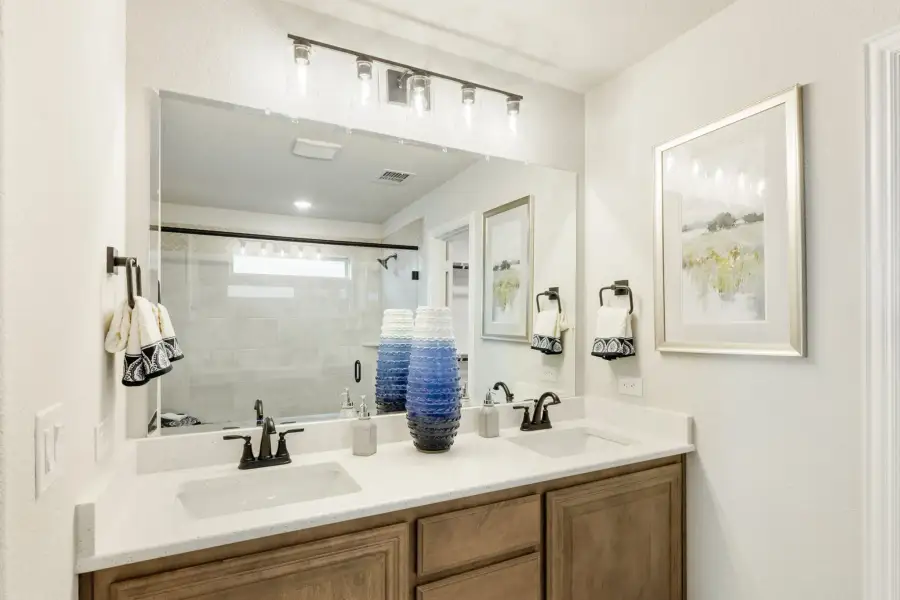 Bathroom with double sink vanity, wood cabinets, white countertop, and large mirror with overhead lighting