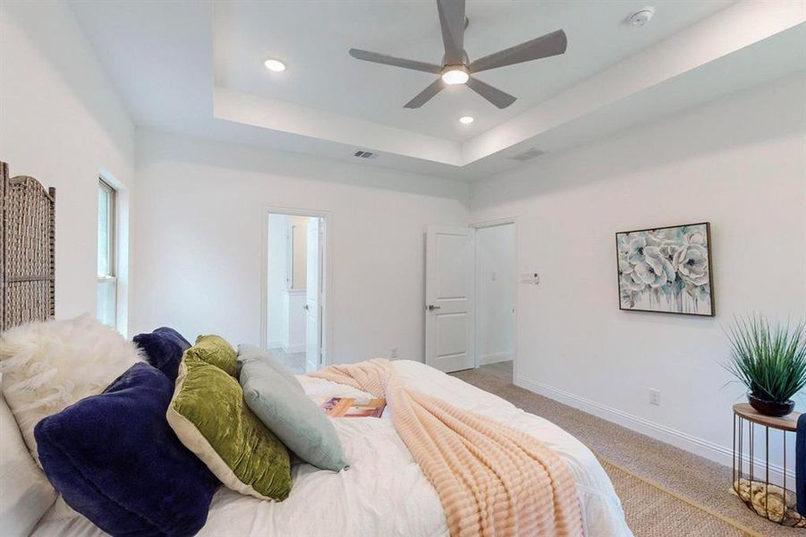 Main Bedroom with ceiling fan, a raised ceiling, connected bathroom, and light carpet