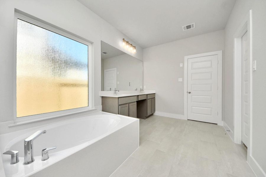 Indulge in a spa-like retreat within the confines of this primary bathroom. Delight in a spacious walk-in shower enveloped in stylish tile surround, unwind in a separate garden tub adorned with custom detailing.