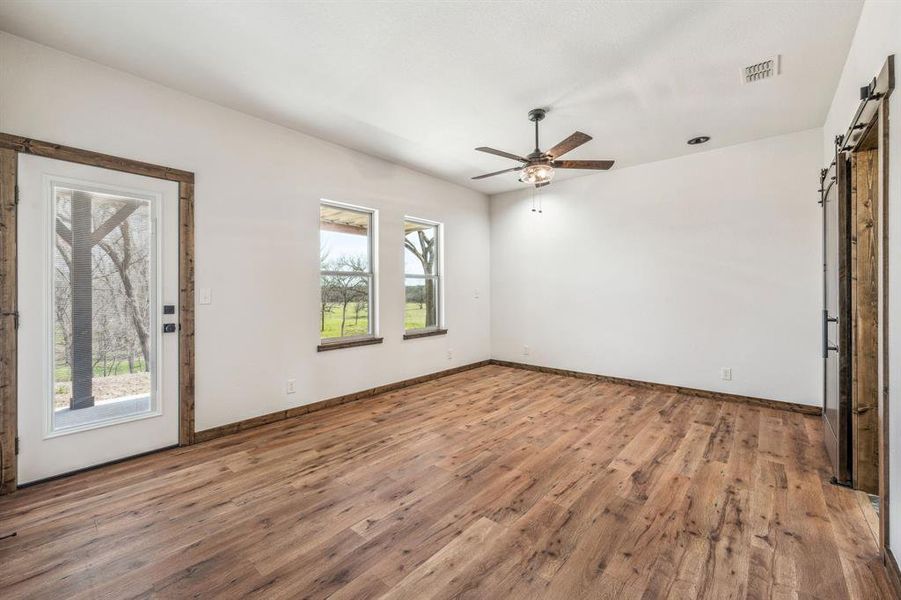 Unfurnished room with baseboards, a barn door, visible vents, a ceiling fan, and wood finished floors