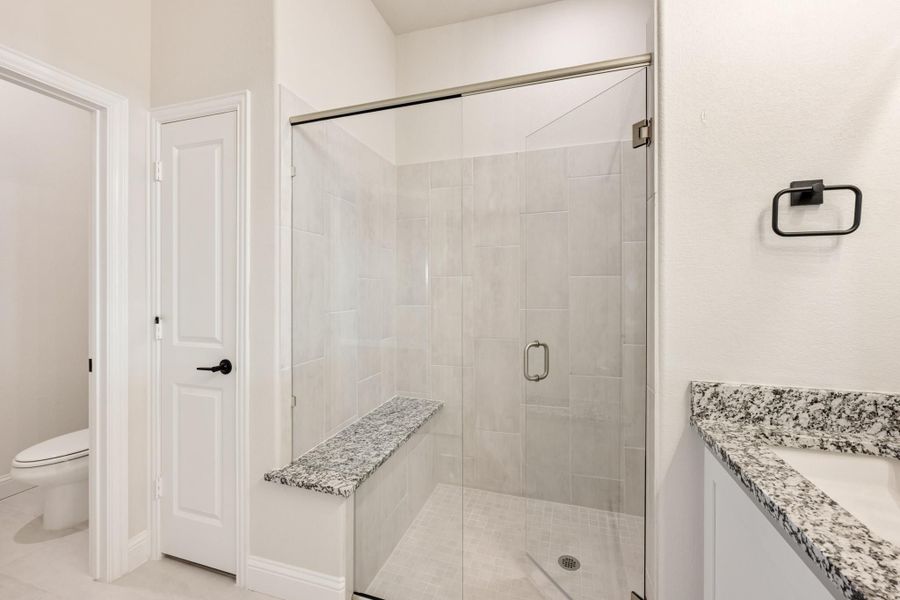 Bathroom with glass-door walk-in shower, granite bench seat, white tile walls, and granite vanity countertop