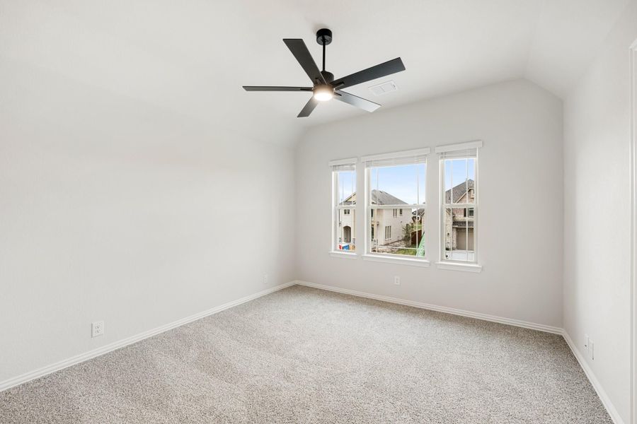 Empty bedroom with vaulted ceiling, black ceiling fan, carpet flooring, and triple windows