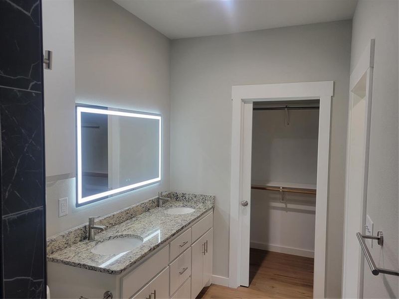 Bathroom vanity featuring dual under-mount sinks, a granite countertop, and a back-lit mirror