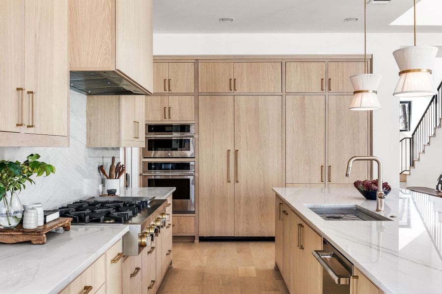 Kitchen with light wood finish cabinetry, light stone countertops, decorative light fixtures, and light wood-type flooring