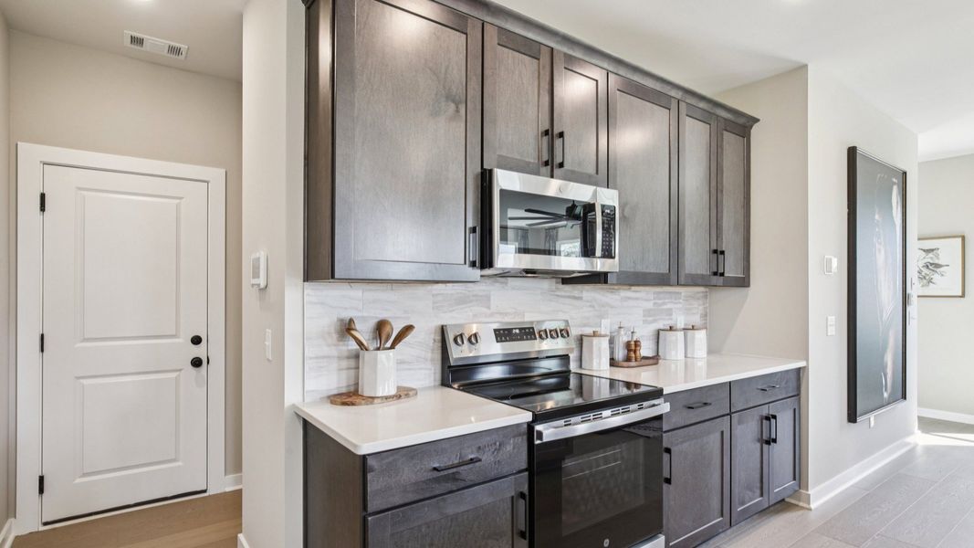 Kitchen with stained gray cabinetry, white quartz countertop, and light tile backsplash