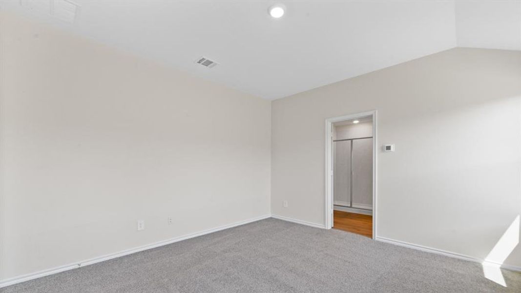 Spacious room featuring vaulted ceilings, neutral-toned walls, and plush grey carpeting