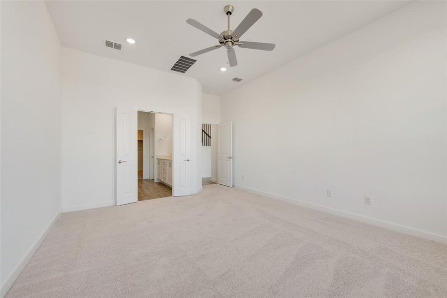 Unfurnished bedroom featuring ceiling fan, ensuite bathroom, and light colored carpet