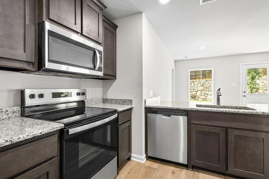 Kitchen featuring stainless steel appliances, dark brown cabinetry, light wood-style floors, light stone counters, and a peninsula