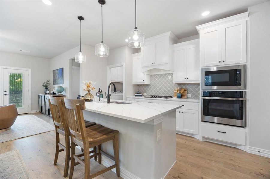Kitchen with decorative backsplash, stainless steel appliances, a breakfast bar area, light wood-style floors, and light quartz countertops