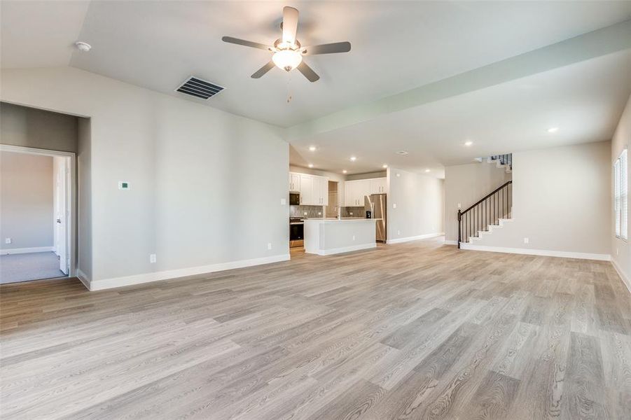 Unfurnished living room with a ceiling fan, light wood-style flooring, stairs, recessed lighting, and vaulted ceiling Unfurnished living room with a ceiling fan, light wood-style flooring, stairs, recessed lighting, and vaulted ceiling