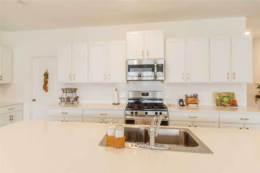 Gourmet kitchen with stainless steel appliances, elegant white cabinetry, light wood-inspired flooring, quartz countertops, and a beautifully detailed backsplash—perfect for cooking and entertaining.