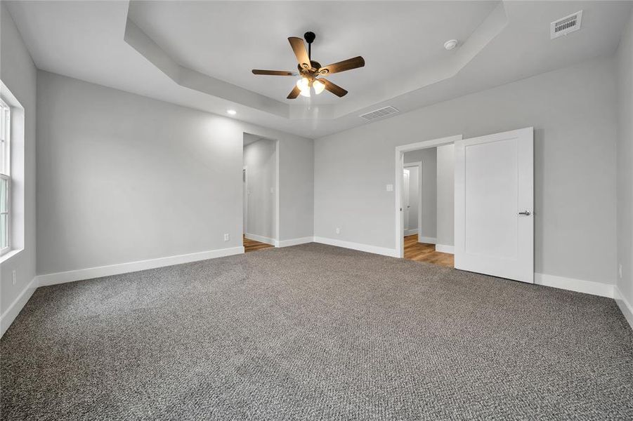 Unfurnished bedroom with ceiling fan, a tray ceiling, and carpet