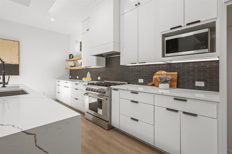 Kitchen featuring sink, custom range hood, light wood-type flooring, white cabinetry, and stainless steel appliances