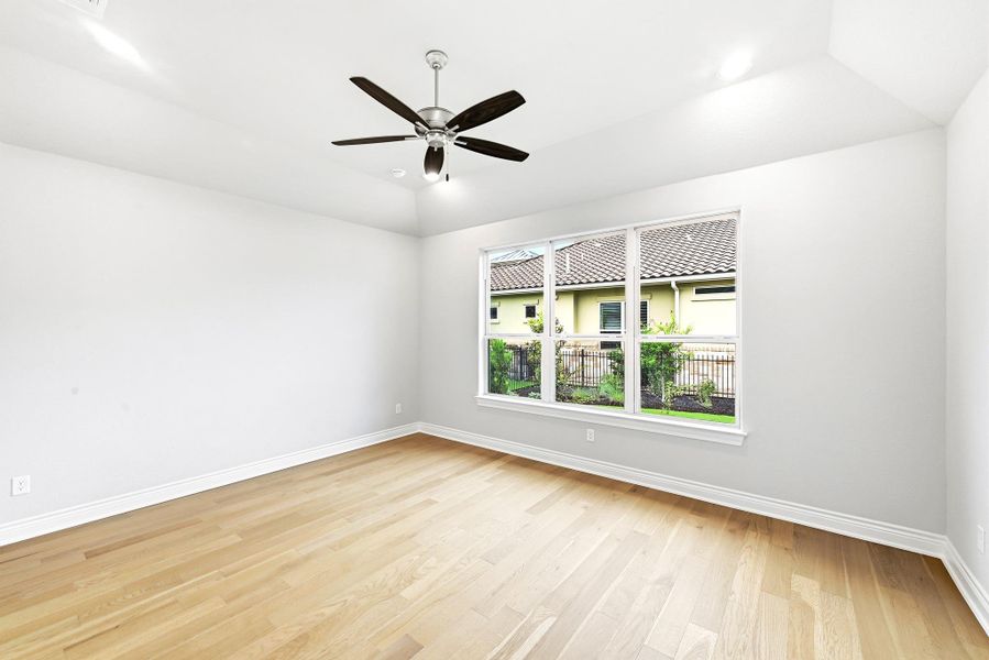 Spacious room featuring wood-finish flooring, a large multi-pane window, and a ceiling fan